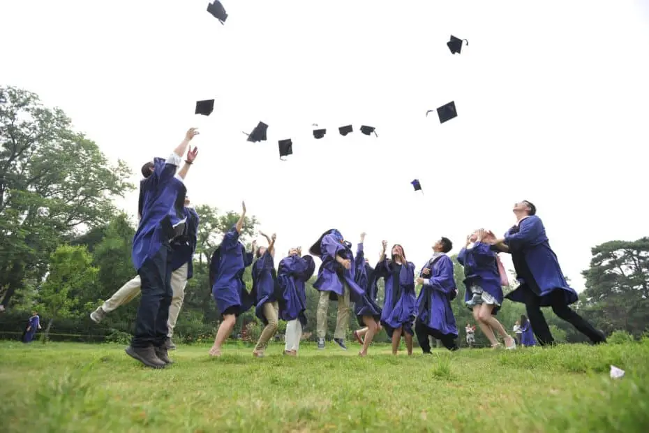 A dozen graduates in a field throwing their caps into the air